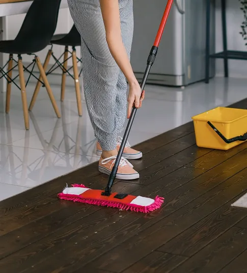 Mopping a shiny dark wooden floor with a flat mop next to a yellow bucket